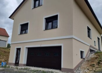 Nově postavený dům se žlutou fasádou, tmavě hnědými okny a dveřmi, doplněný o vjezd do garáže